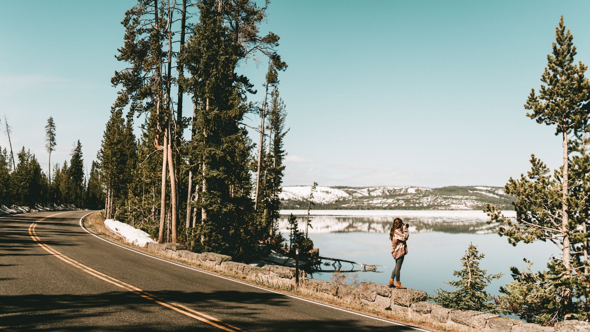 Kobieta robi zdjęcia nad jeziorem Yellowstone zimą, w tle góry i śnieg